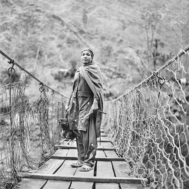 Kobieta z&nbsp;kogutem na&nbsp;wisz�cym mo�cie w&nbsp;okolicach miejscowo�ci Tatopani (tytu�: &bdquo;Kobiety&rdquo;).