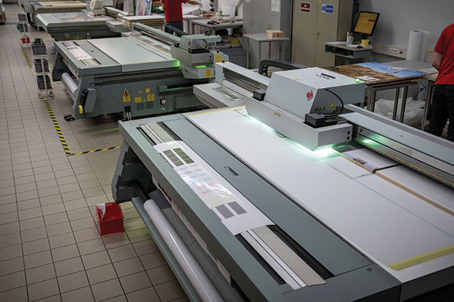 Maszyna do druku bezpośredniego z utwardzaniem w świetle UV. Na tych ­maszynach drukuje się wszystkie CEWE FOTOOBRAZY i dekoracje ścienne. Na zdjęciu widać drukowanie CEWE FOTOOBRAZU na drewnie. 