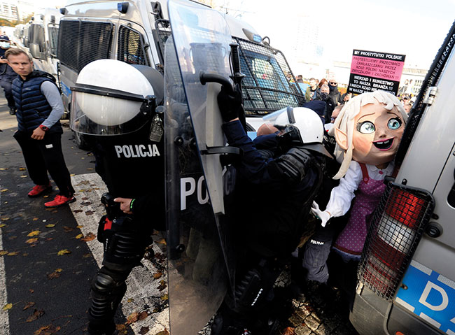 Polska policja w strojach bojowych zatrzymuje demonstrantów rozzoszczonych nowymi ograniczeniami majcymi na celu zwalczanie pandemii koronawirusa w Warszawie w sobot 24 padziernika 2020 r. Wród protestujcych byli przedsibiorcy, skrajnie prawicowi politycy, kibice i przeciwnicy szczepionek. Protestujcy, wielu bez masek ochronnych, zamali nowe ograniczenie dotyczce gromadzenia si wikszej liczby osób. (fot. AP Photo / Czarek Sokoowski)