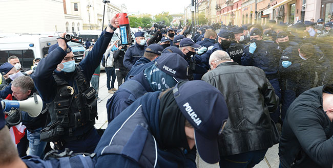 Policjant filmujc odpala gaz pieprzowy przeciwko protestujcym domagajcym si zniesienia ogranicze ekonomicznych podczas pandemii koronawirusa w  Warszawie, sobota, 16 maja 2020 r. (fot. AP Photo / Czarek Sokoowski)