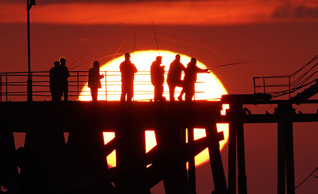 Anglers, hoping to catch mackerel and other fish, cast from the end of Blyth pier in Northumberland as the sun rises over the north east coast of England. Picture date: Wednesday August 4, 2021.  Photograph: Owen Humphreys